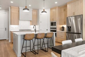 A modern kitchen with a central island, bar stools, stainless steel appliances, and wooden cabinetry. - Vacation Mode 5 Bedroom Townhouse (St. George)