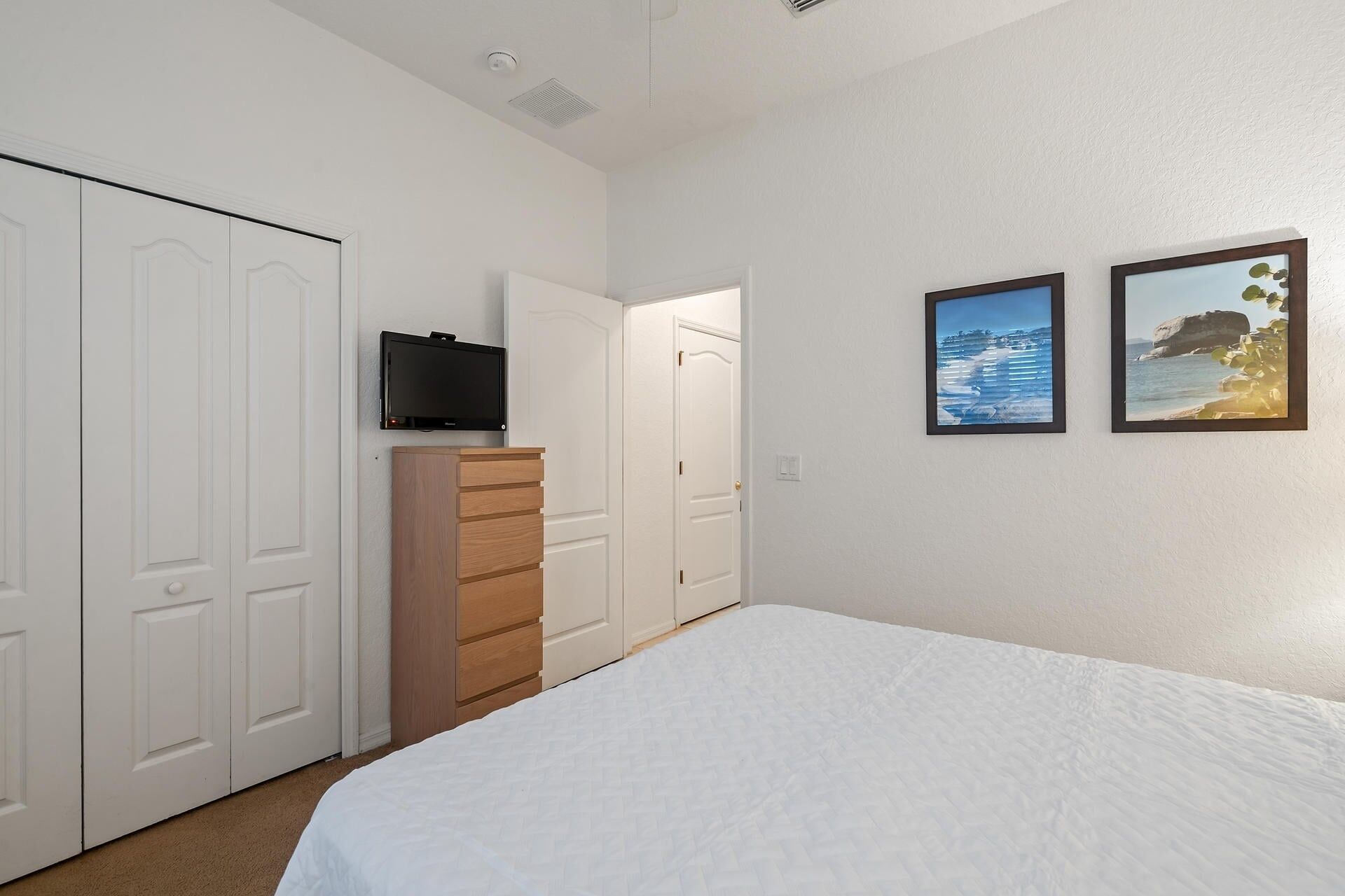 A bedroom with a bed, a dresser, a television, and two framed pictures on the wall.