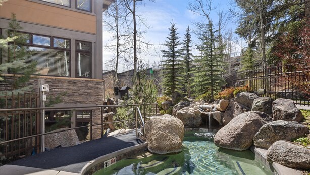 A pool area with large rocks, a stone wall, and a metal railing. - Aw K17 2 Bedroom Condo (Snowmass Village)