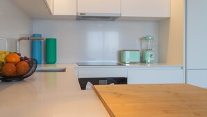 A modern kitchen with a wooden table, a fruit basket, a blender, and a dishwasher. - Calm Luxury w Pool Gym Parking (Lisbon)