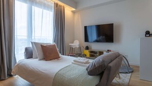 A hotel room with a bed, a TV, a desk, and a view of the city. - Calm Luxury w Pool Gym Parking (Lisbon)