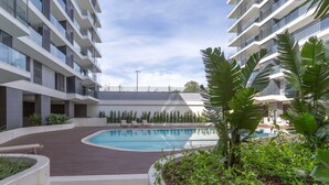 A modern building with a swimming pool, surrounded by greenery and a wooden deck. - Calm Luxury w Pool Gym Parking (Lisbon)