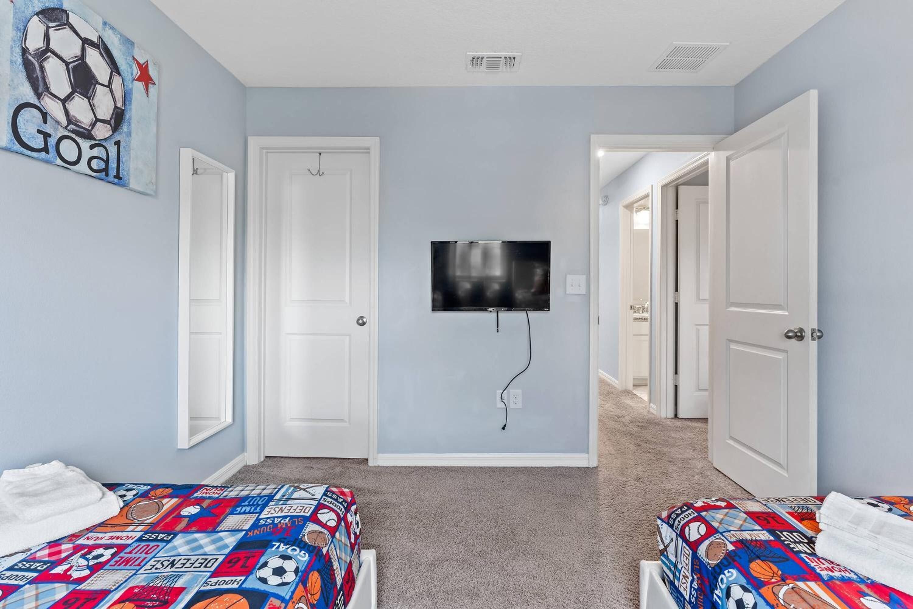 A bedroom with two beds, a TV mounted on the wall, and a door leading to another room.