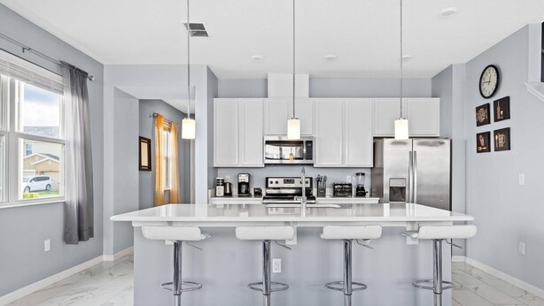 A modern kitchen with white cabinets, stainless steel appliances, and a central island with bar stools. - 4BR Grill Resort Pool Kids Rooms Near Disney 5129 (Kissimmee)