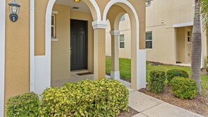 A building with a beige facade, white arches, a black door, and a small garden with bushes. - 4BR Grill Resort Pool Kids Rooms Near Disney 5129 (Kissimmee)