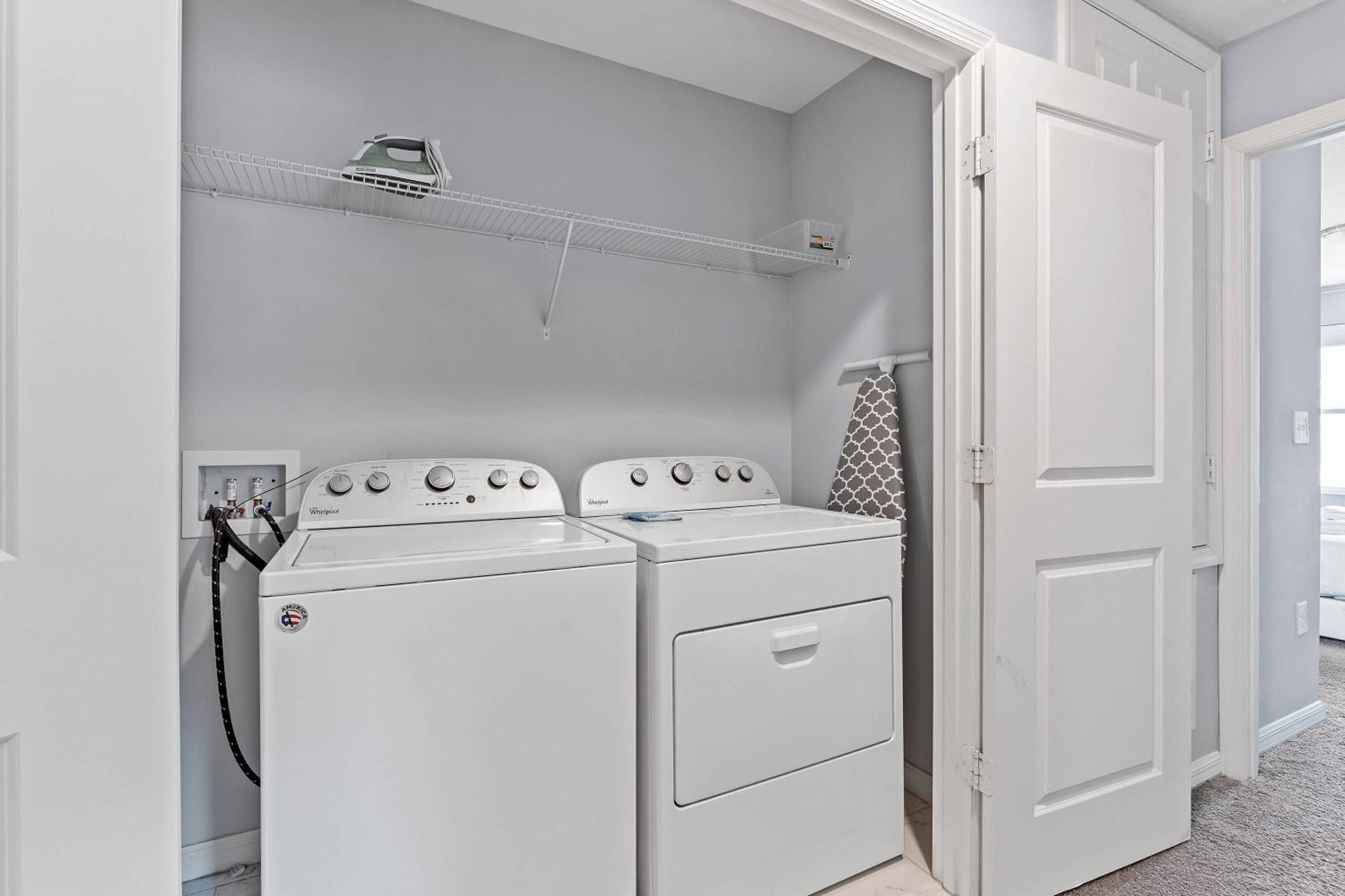 A laundry room with two white Whirlpool washers, a shelf above, and a door to the right.