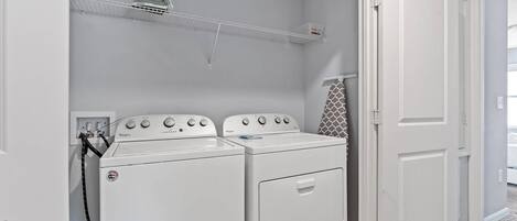 A laundry room with two white Whirlpool washers, a shelf above, and a door to the right.