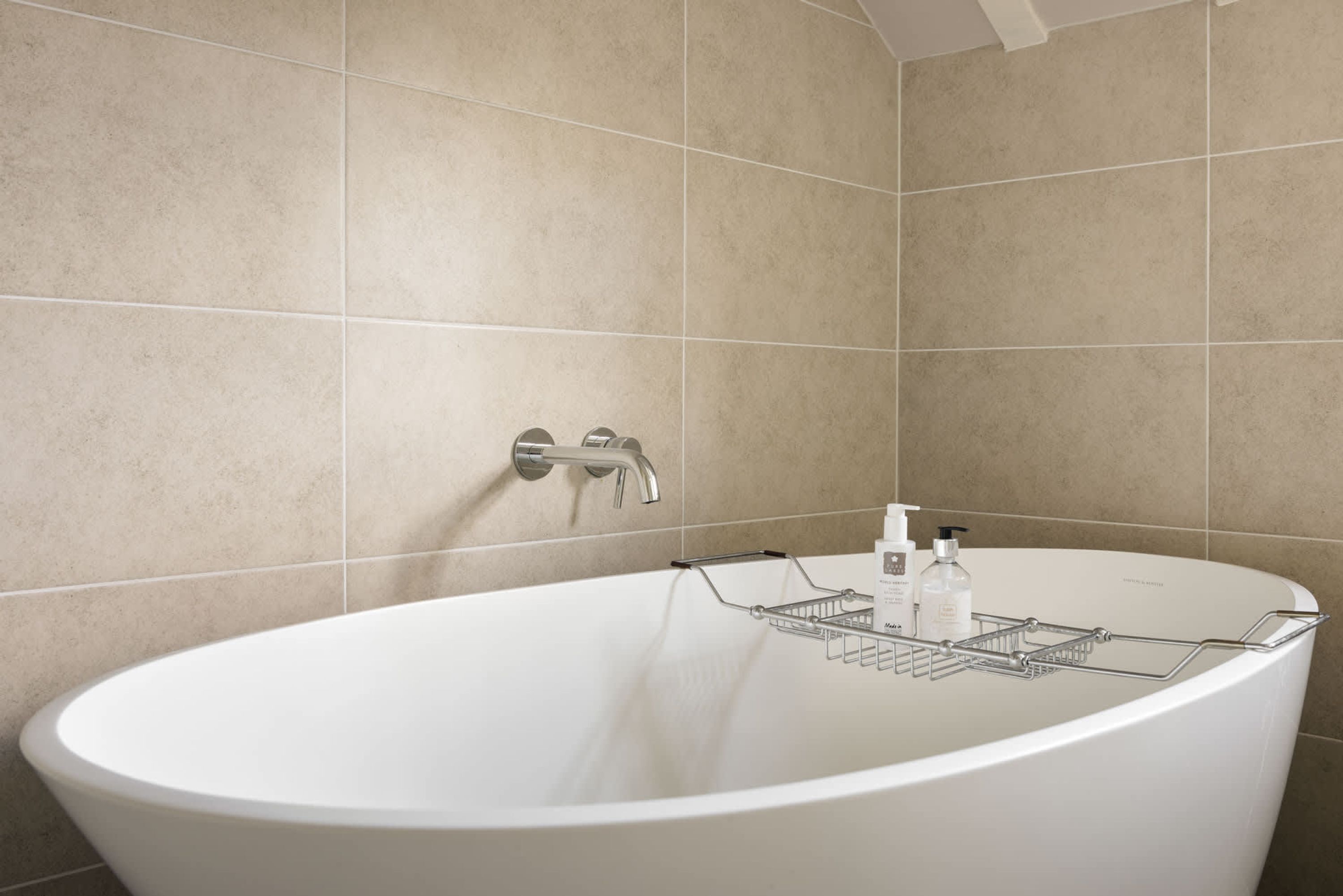 A modern bathroom with a freestanding bathtub, a wall-mounted faucet, and a metal bath tray with toiletries.