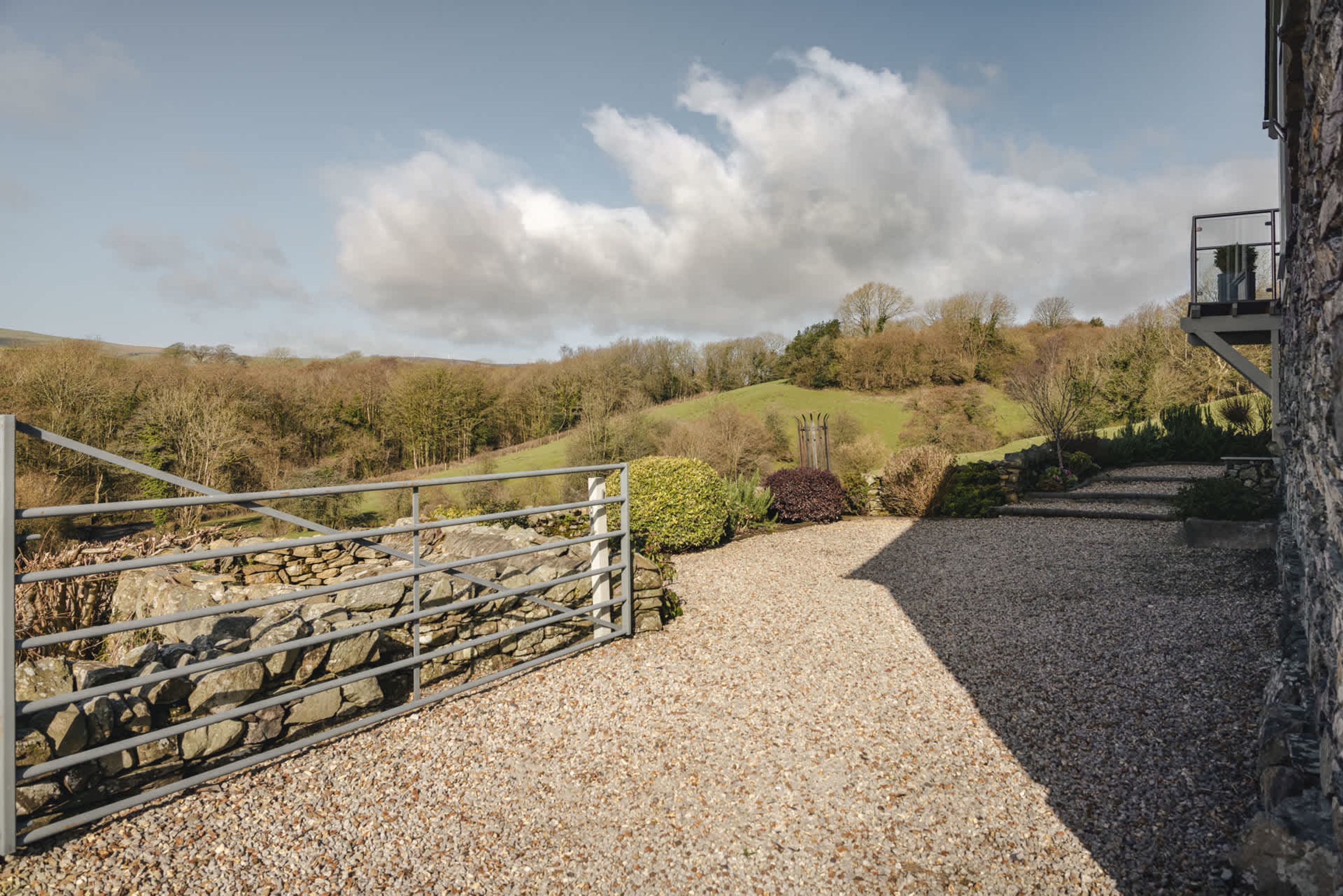 A gravel path leading to a stone wall, a metal gate, and a stone building with a balcony.