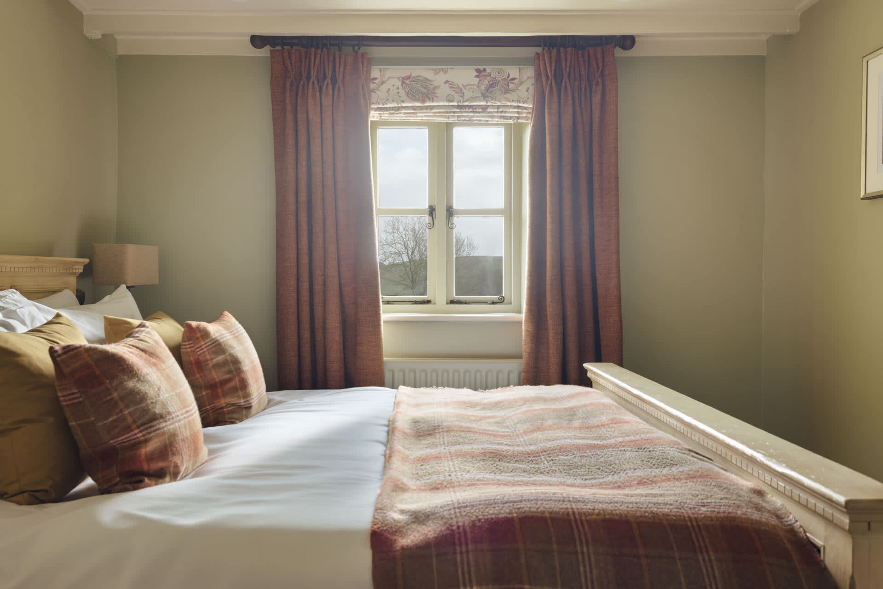 A bedroom with a bed, pillows, a window with curtains, and a radiator.
