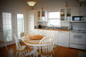 A kitchen with white cabinets, a wooden dining table, and chairs. - Your Coastal Retreat Awaits at Giddy's Get Away (N Topsail Beach)