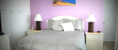 A bedroom with a bed, two bedside tables, a nightstand, a painting on the wall, and a door.