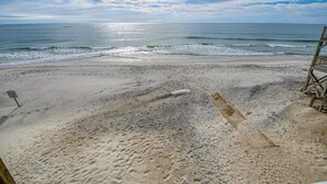Une plage avec une promenade en bois menant à l’eau, un poste de surveillance pour les sauveteurs et un panneau indiquant les règles à respecter sur la plage.