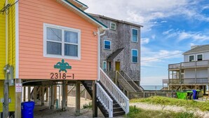 Une maison de plage avec un escalier menant à une terrasse, une jetée donnant sur la plage et un panneau indiquant « La maison de plage ».
