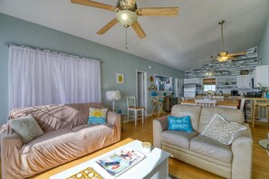A living room with a sofa, armchair, and coffee table, a kitchen in the background, and a ceiling fan. - The Beach Peach – Oceanfront Escape with Panoramic Views (North Topsail Beach)