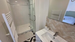 Un baño moderno con cabina de ducha de vidrio, un lavamanos blanco y un suelo con estampado tipo espiga.
