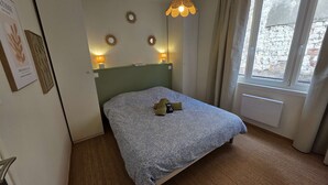 Una habitación de hotel con cama, dos lámparas de pared, una ventana con cortinas y un radiador.