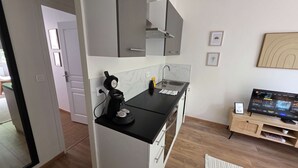 Cocina moderna con encimera negra, cafetera y fregadero. Un televisor sobre un mueble de madera a la derecha.