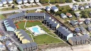 An aerial view of a coastal residential area with houses, a large pool, and a beach. - Oceanfront Escape at Surf Condo 814 – Relaxation Starts Here (Surf City)