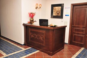 A reception desk with a laptop, a vase with flowers, and a framed artwork on the wall.
