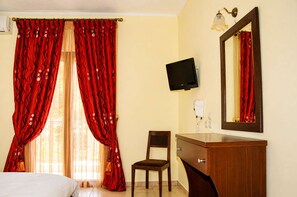 A hotel room with a bed, a wooden chair, a TV, a mirror, and a bathroom with a sink and toilet.