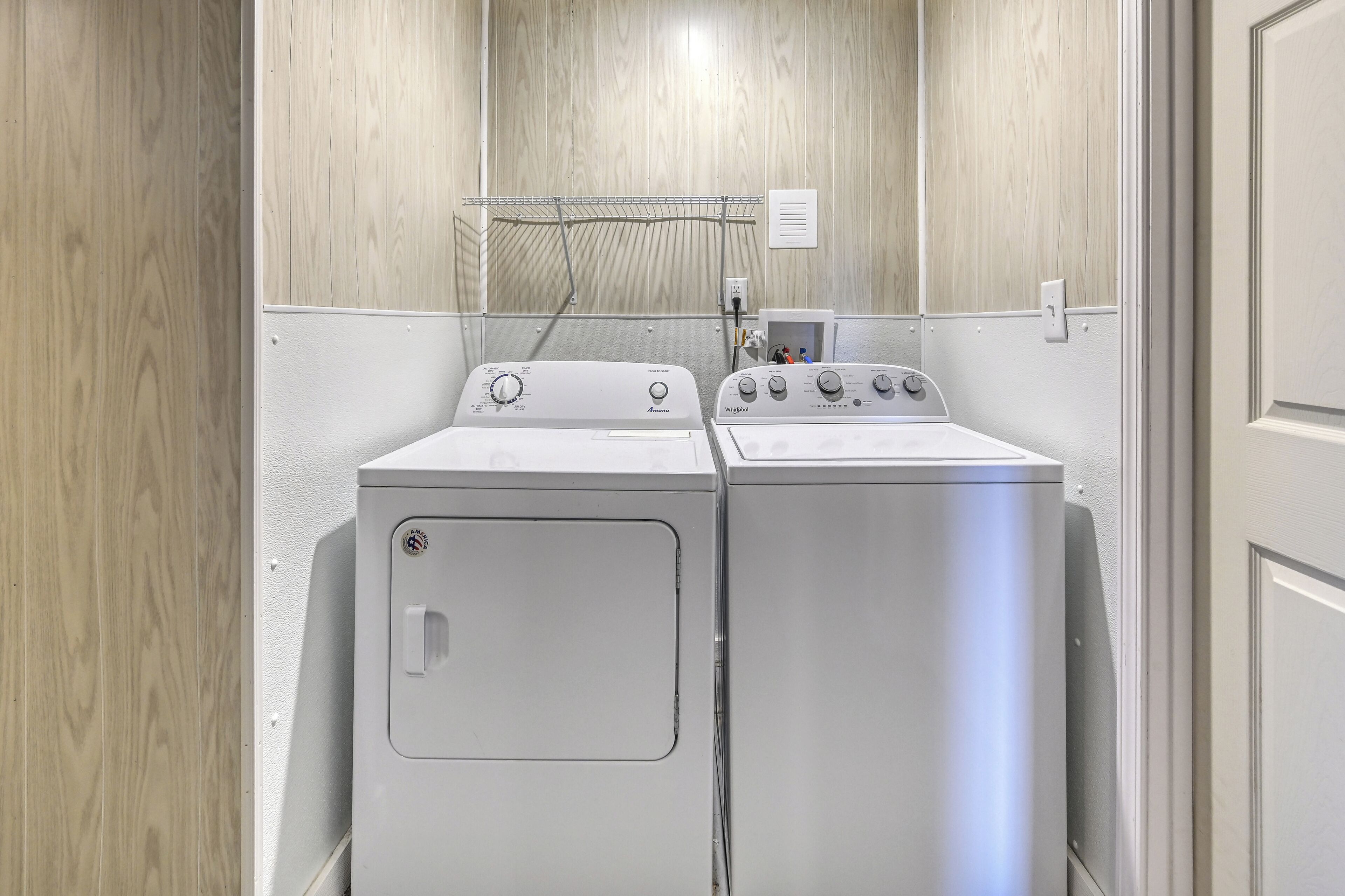 A laundry room with two stacked washers and dryers, a metal drying rack, and a wall-mounted electrical outlet.