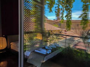 Ein Zimmer mit Bett, Fenster und Blick auf Gebäude und Bäume.