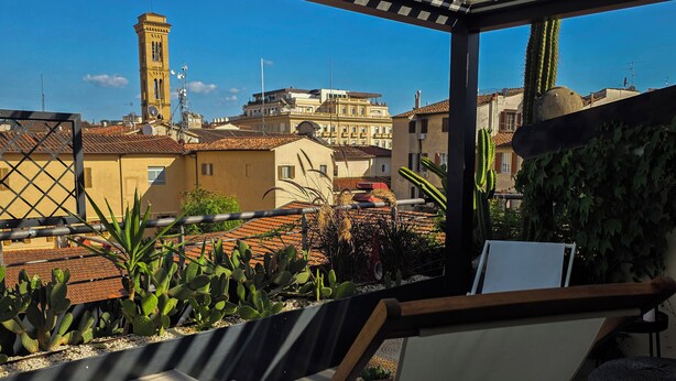 Une terrasse avec une chaise, des cactus et une vue sur des bâtiments, dont une tour.