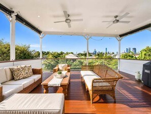 A covered outdoor area with a wooden deck, two sofas, a table, and a grill. - West End Oasis: 4BR w/ Full amenities and Pool (Brisbane)
