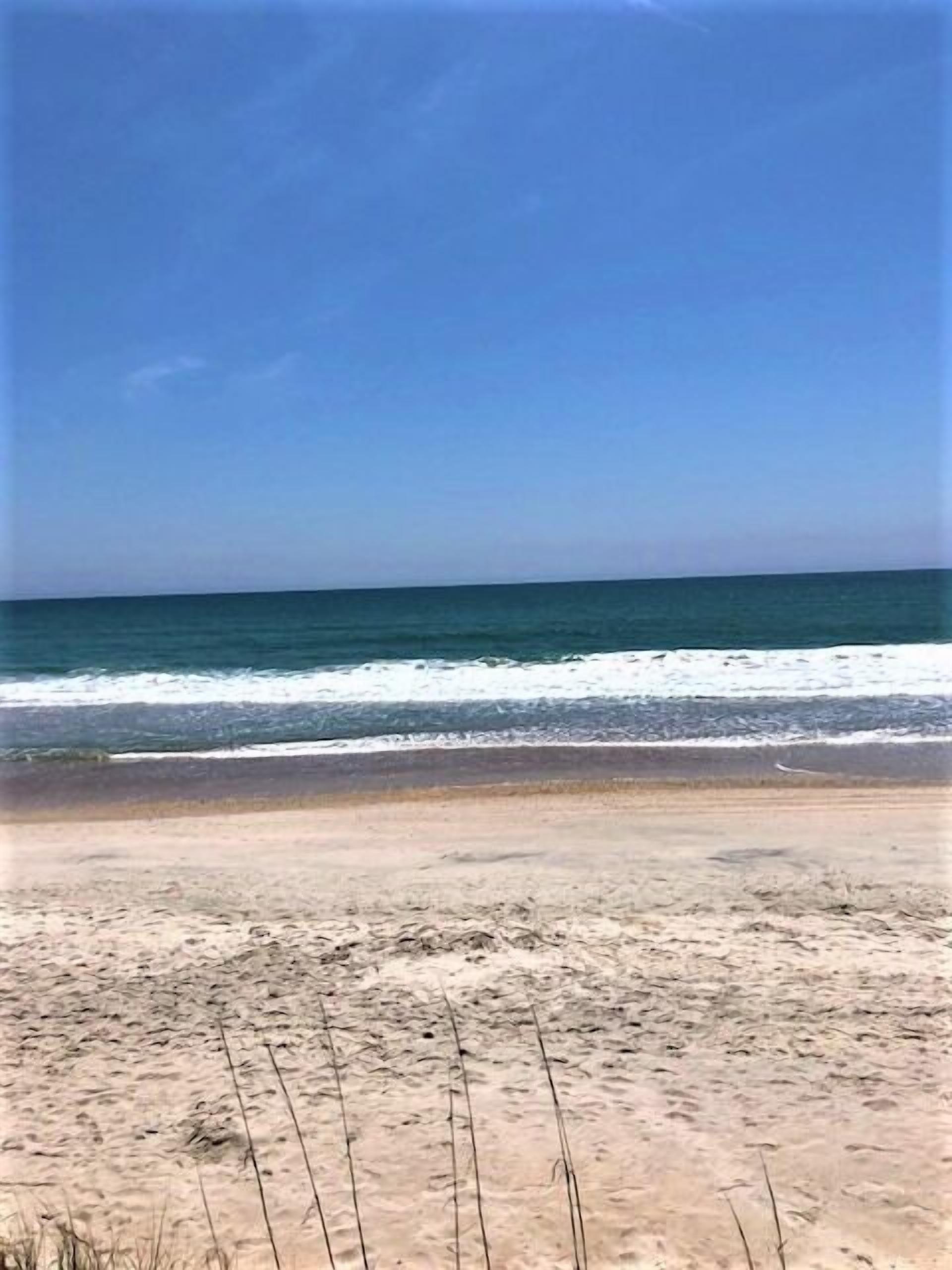 A beach with sand and ocean waves under a clear sky.