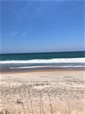 Ein Strand mit Sand und Wellen unter blauem Himmel.