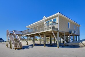 A two-story house with a balcony on the second floor, a wooden staircase leading to the balcony, and a sandy beach in the background. - Oceanfront Bliss on Topsail Island (Surf City)