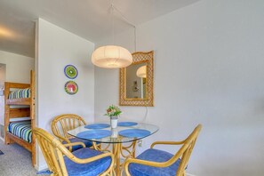 A dining area with a round glass table, blue cushioned chairs, a hanging light fixture, and a mirror with a decorative frame. - Your Oceanfront Escape awaits in Surf City - Surf Condo 713 (Holly Ridge)