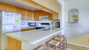 A kitchen with wooden cabinets, a white countertop, a microwave, a stove, and a sink. - Oceanfront Condo – Surf City, NC (Surf City)