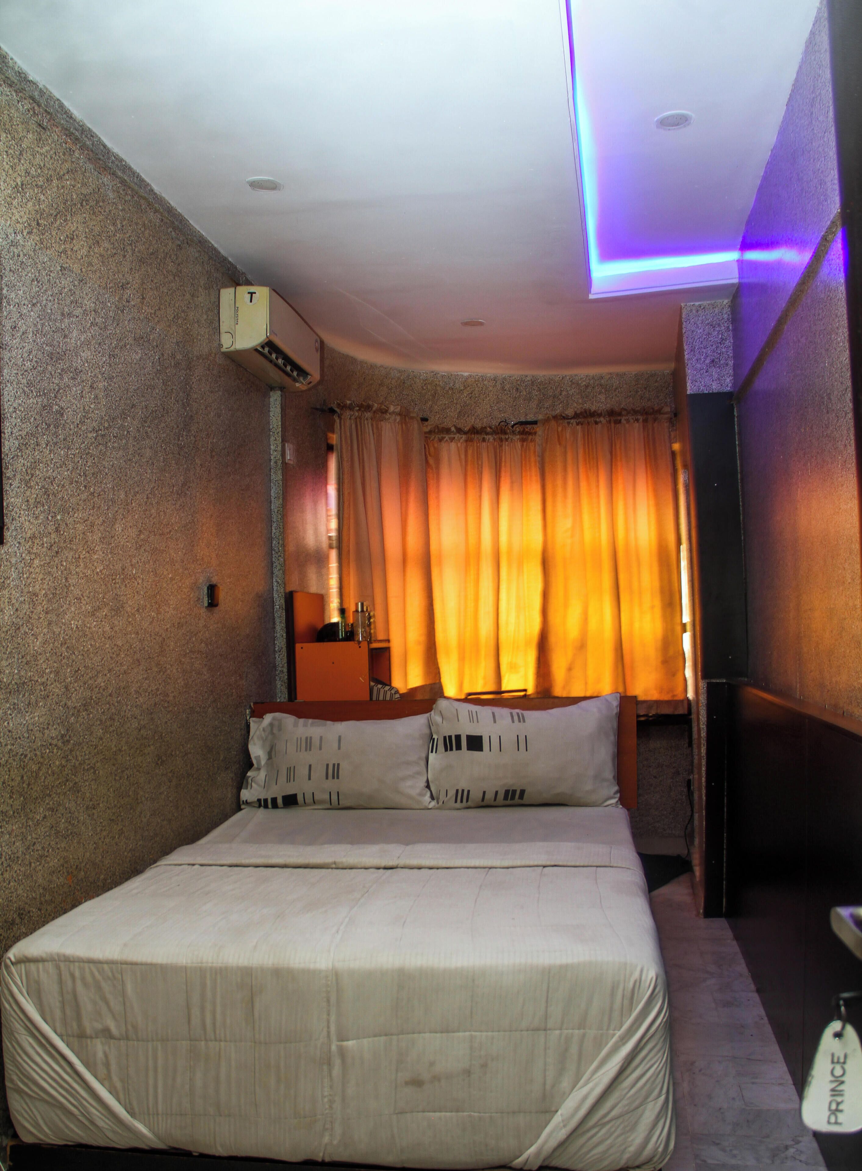 A bedroom with a bed, curtains, an air conditioning unit, and a bedside table.