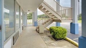 A building with a covered walkway, a staircase, and a small bush.