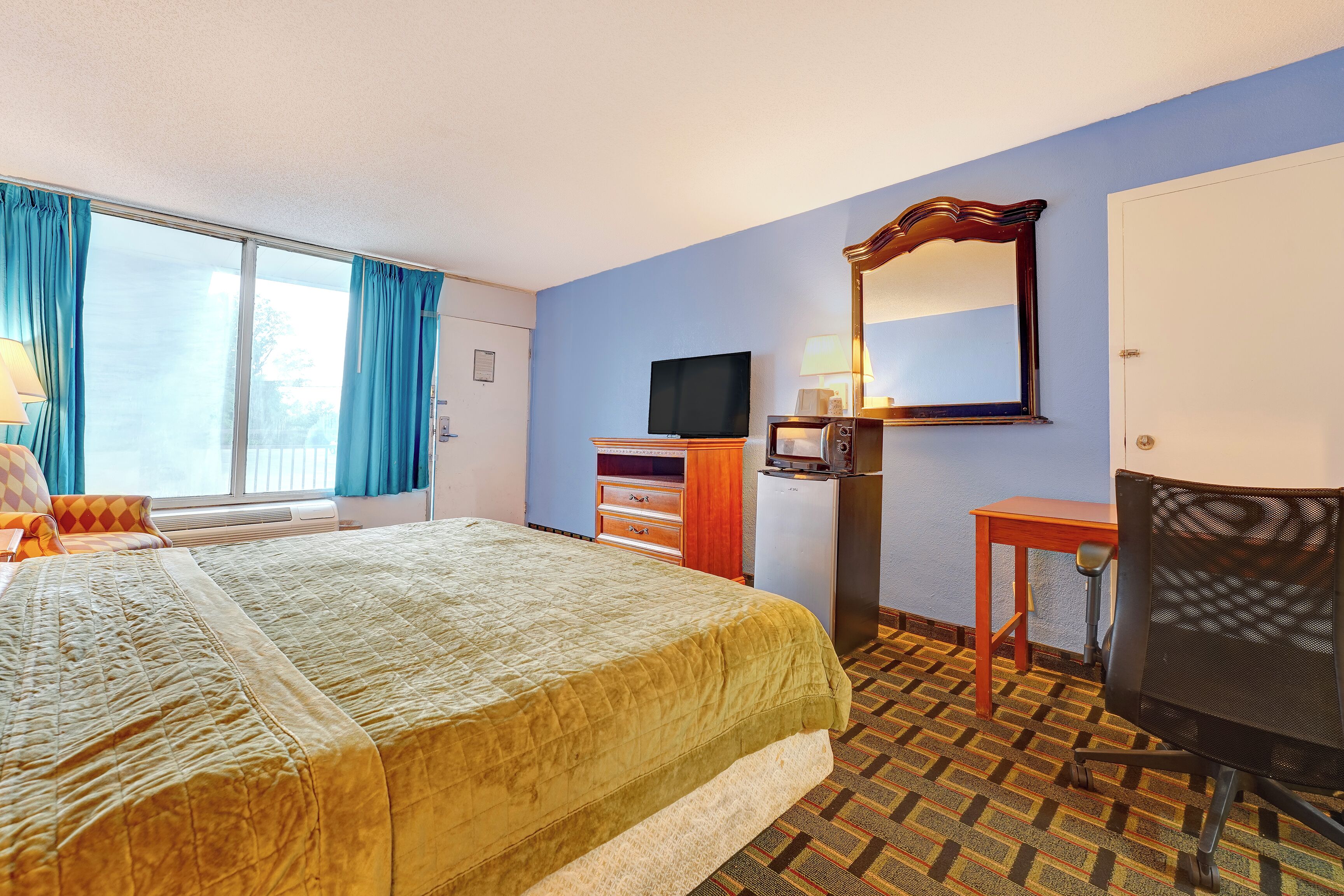 A hotel room with a bed, a television, a desk, a chair, and a large window with curtains.