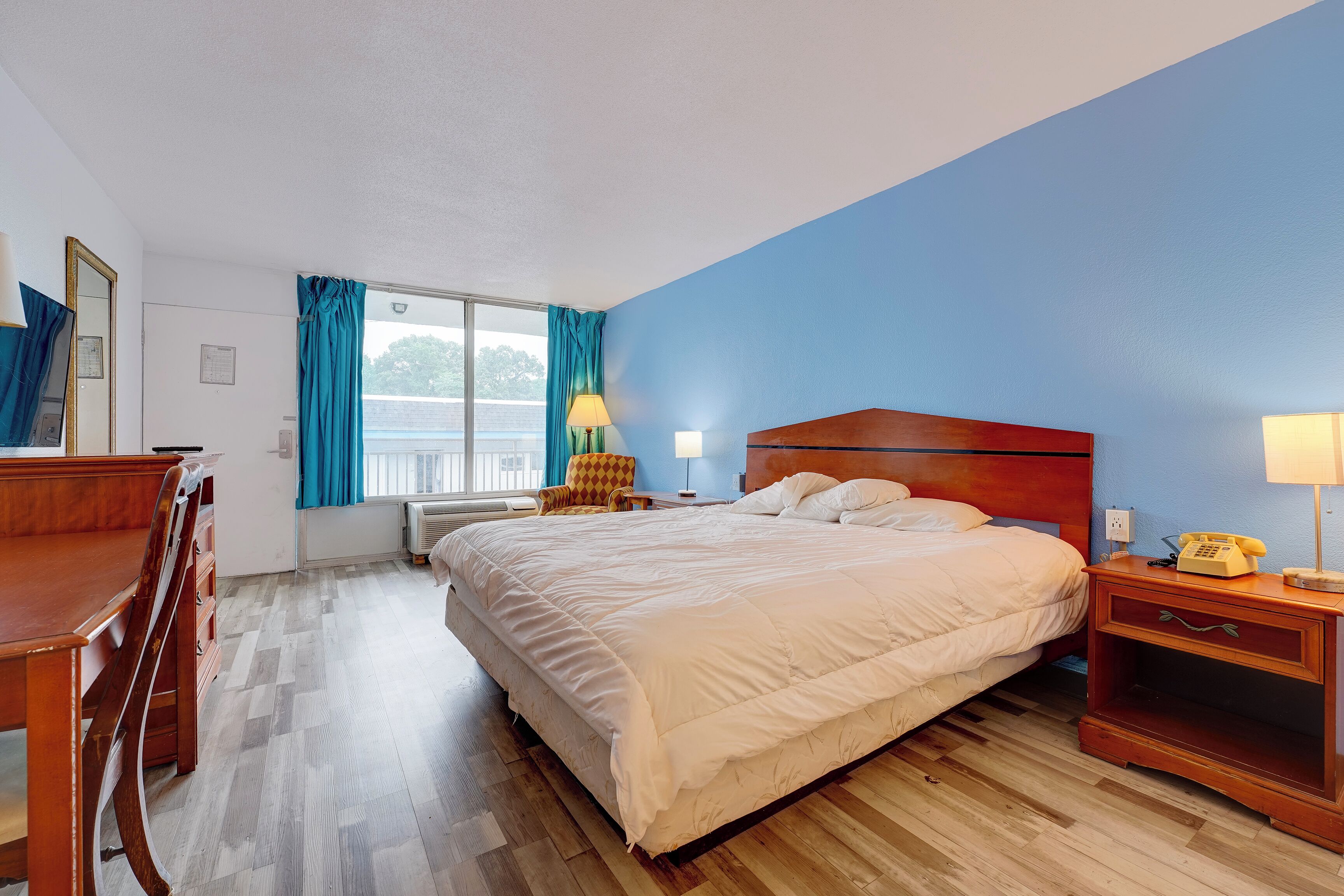 Habitación de hotel con cama, escritorio, silla, mesita de noche, lámpara y teléfono.