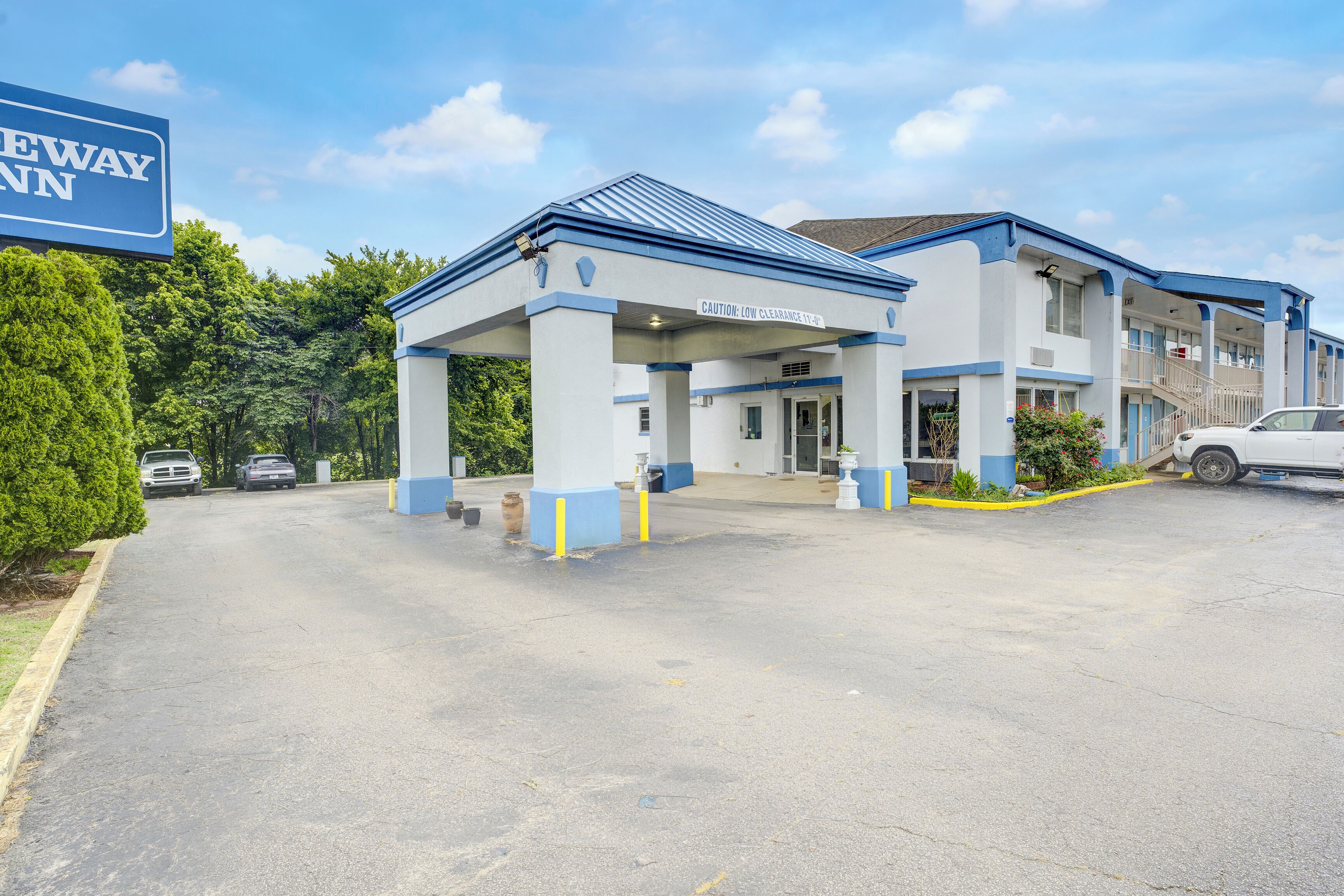 Um hotel com entrada coberta, uma placa indicando altura máxima e um estacionamento com vários carros.