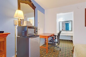 A compact hotel room with a kitchenette, a single bed, a desk with a chair, a window with curtains, and a patterned floor. - Ole South Inn Jackson I 40 TN (Denmark)