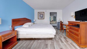 A hotel room with a bed, wooden dresser, desk, chair, and a television.