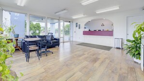 A spacious office with a modern design, featuring a reception desk, a seating area with a sofa and chairs, and large windows providing natural light.