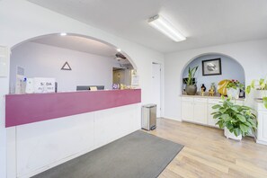 A reception area with a counter, a trash bin, and a seating area with a table and chairs. - Ole South Inn Jackson I 40 TN (Denmark)