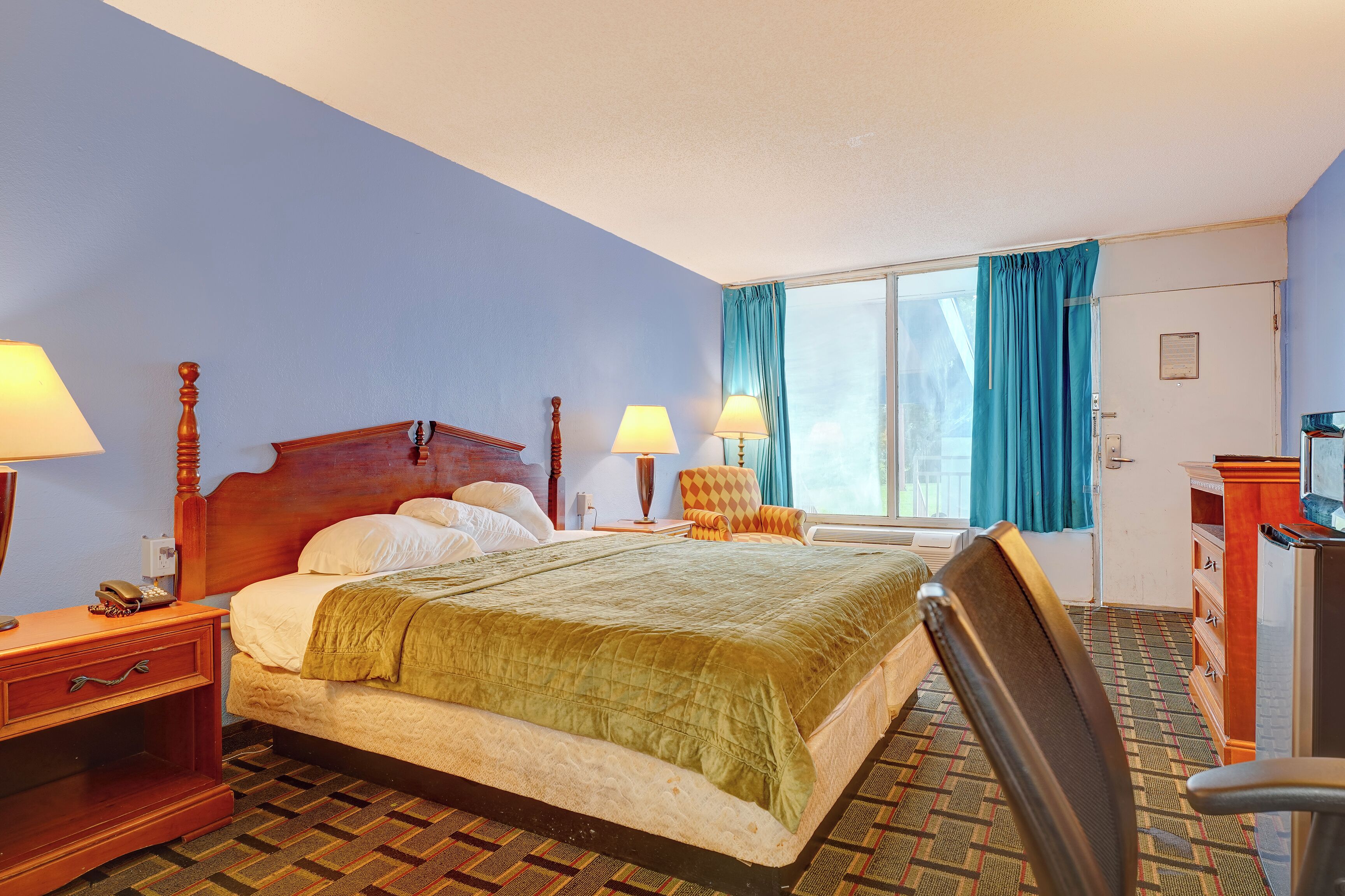Een hotelkamer met een bed, twee bedlampen, een stoel, een bureau en een raam met gordijnen.