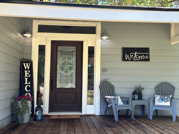 A house entrance with a dark brown door, a welcome sign, and two Adirondack chairs on the porch.