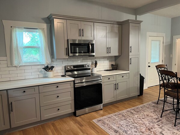 A kitchen with white cabinets, a stainless steel stove, a microwave, and a window with curtains.