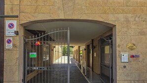 A gated entrance to a building with a stone facade, a metal gate, and various signs including a no parking sign and a fire exit sign. - Stylish & Cozy Apartment in the Center (Firenze)