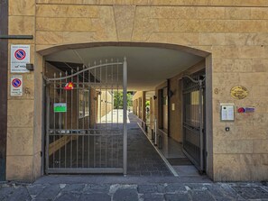 Ein begrenzter Zugang zu einem Gebäude mit einer Steinaußenwand, einem Metallgittertor und verschiedenen Schildern, darunter ein Parkverbotsschild und ein Feuerausgangsschild.