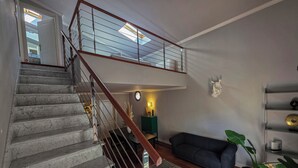 A staircase with a wooden handrail leading to a mezzanine, a dark-colored sofa, a round coffee table, and a potted plant. - Stylish & Cozy Apartment in the Center (Firenze)