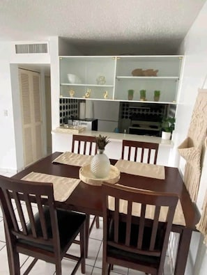 Ein Essbereich mit Holztisch und Stühlen, im Hintergrund eine Küche und eine weiße Decke.